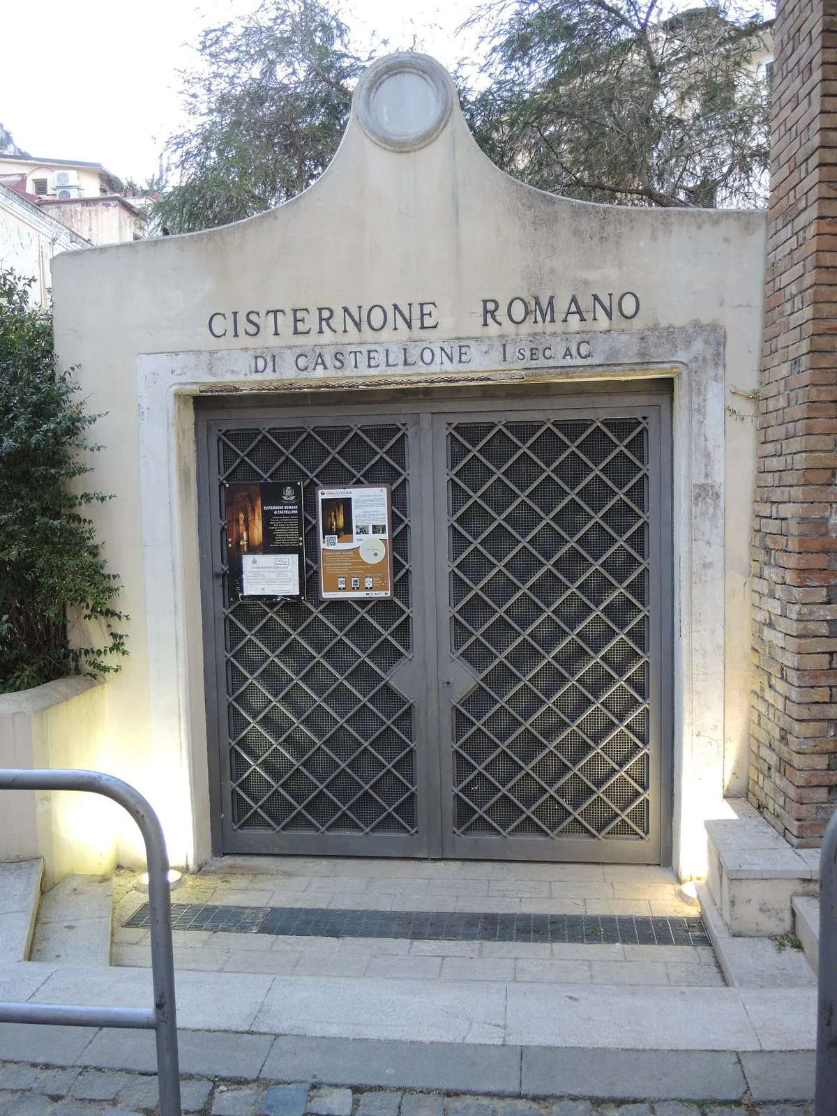Ingresso del Cisternone Romano di Castellone a Formia, portale chiaro con cancello a grata e scritta incisa