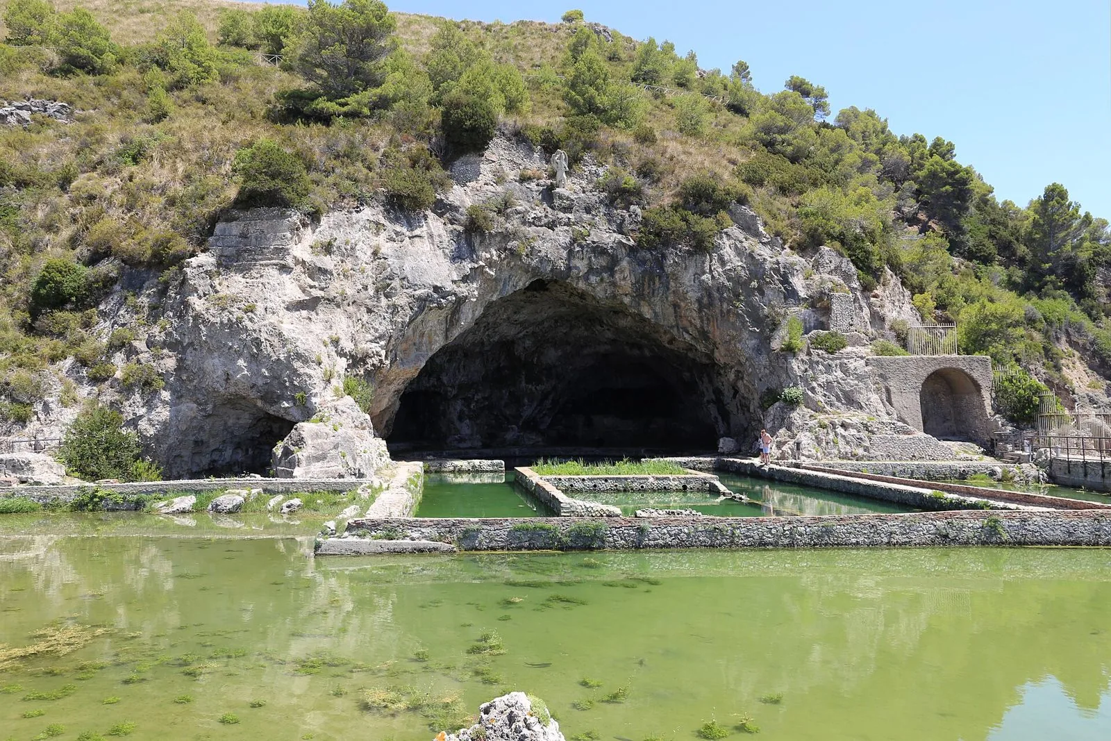 La grotta della Villa di Tiberio a Sperlonga con la grande vasca d'acqua in primo piano e la collina verde sopra l'ingresso