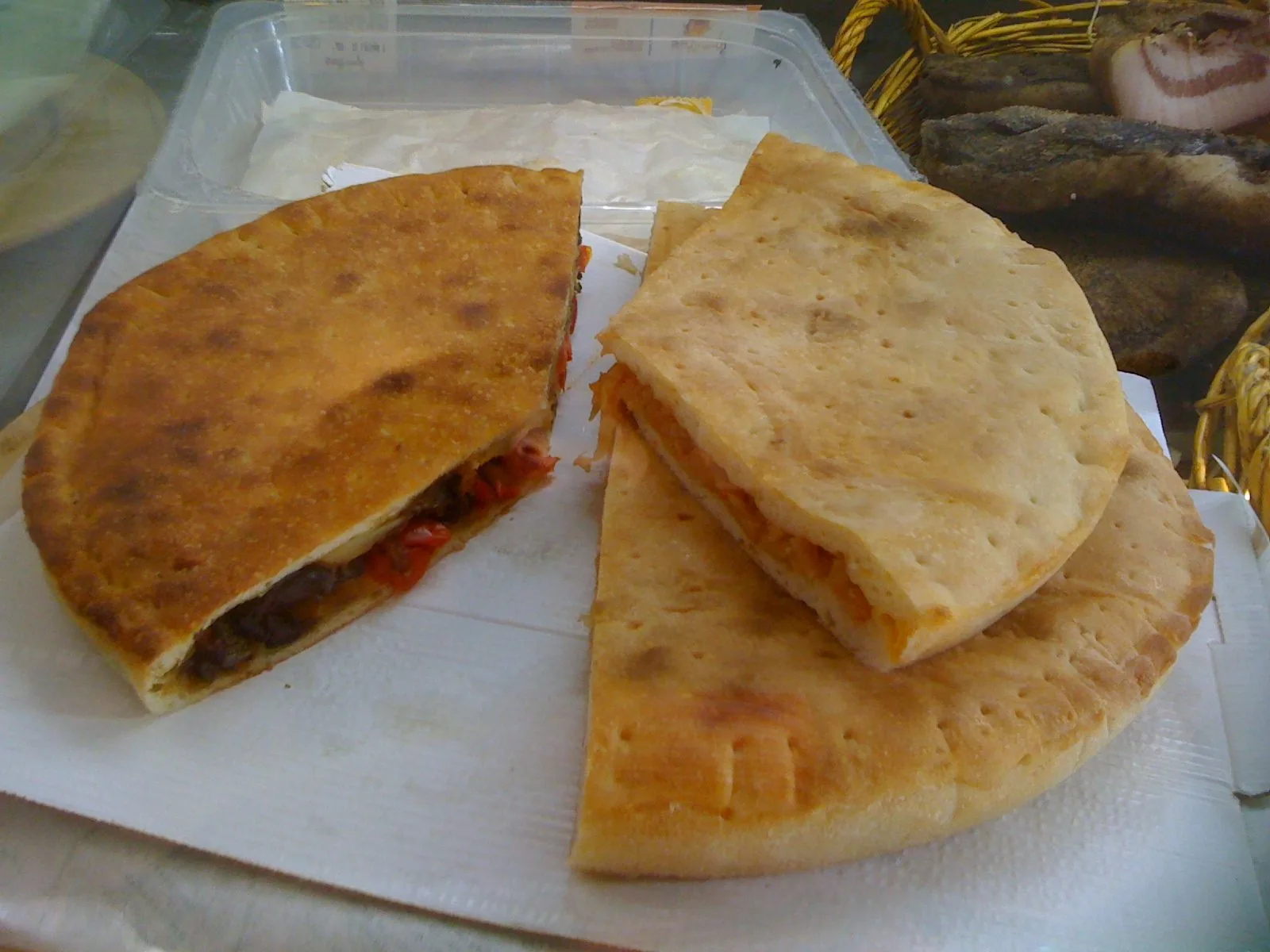 Due tielle di Gaeta tagliate a spicchi, una con ripieno di olive e pomodorini e una con ripieno rosso, su carta da forno