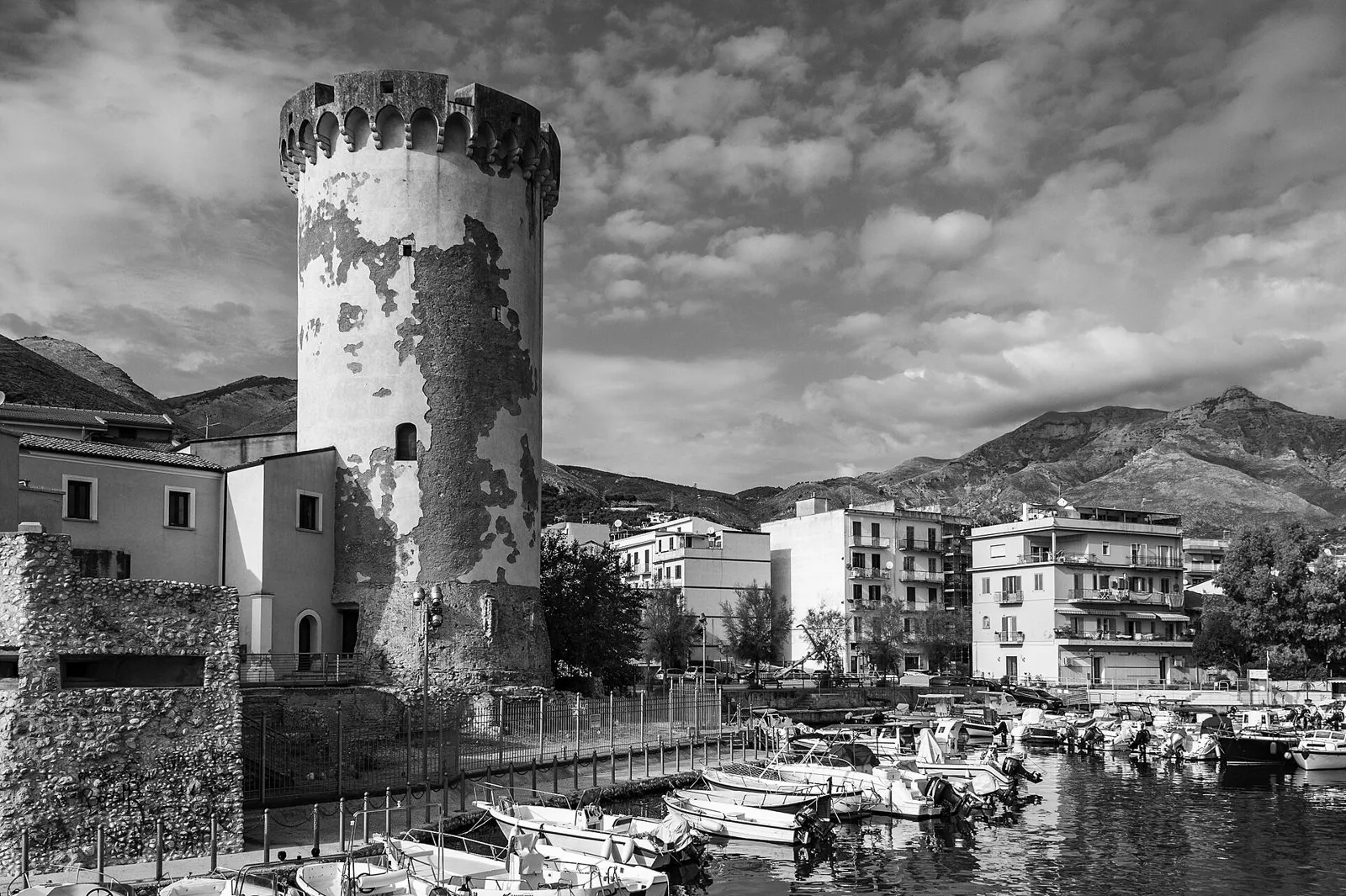 La Torre di Mola a Formia, torrione cilindrico medievale affacciato sul porticciolo con barche, in bianco e nero